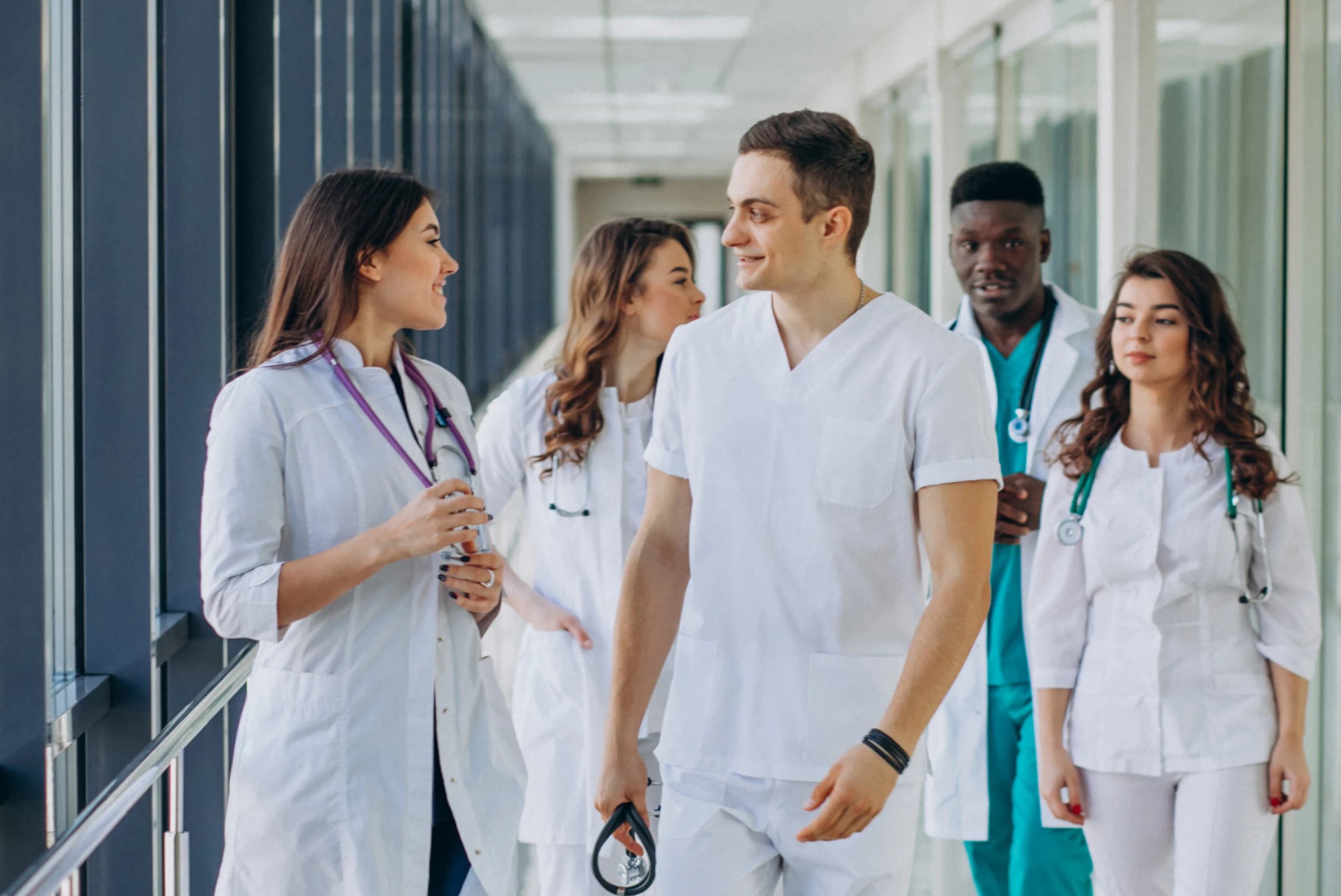 Team of travel nurses in scrubs and lab coats walking together through a bright hospital corridor